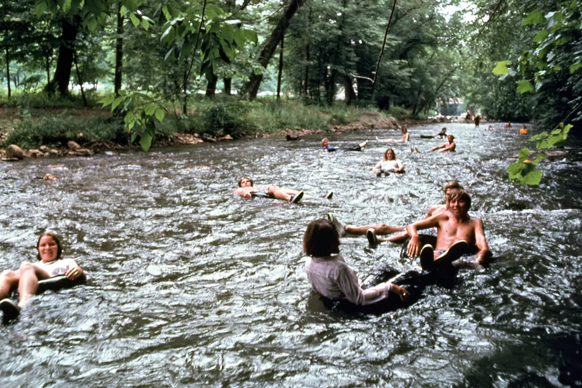 People enjoying a summer day tubing down a scenic river surrounded by lush green trees.