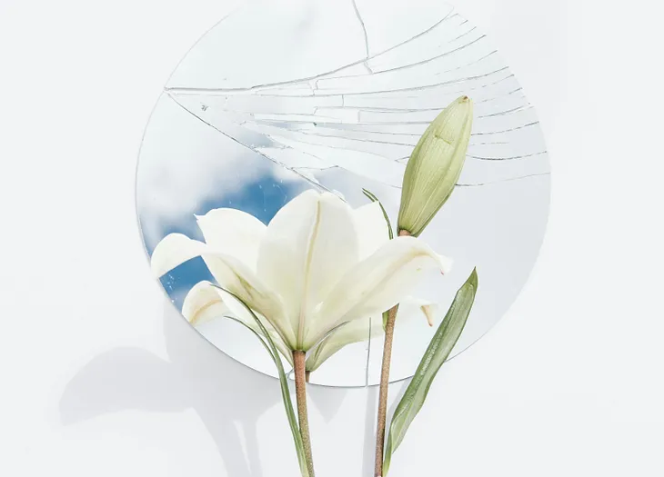 White lilies in front of a cracked round mirror.