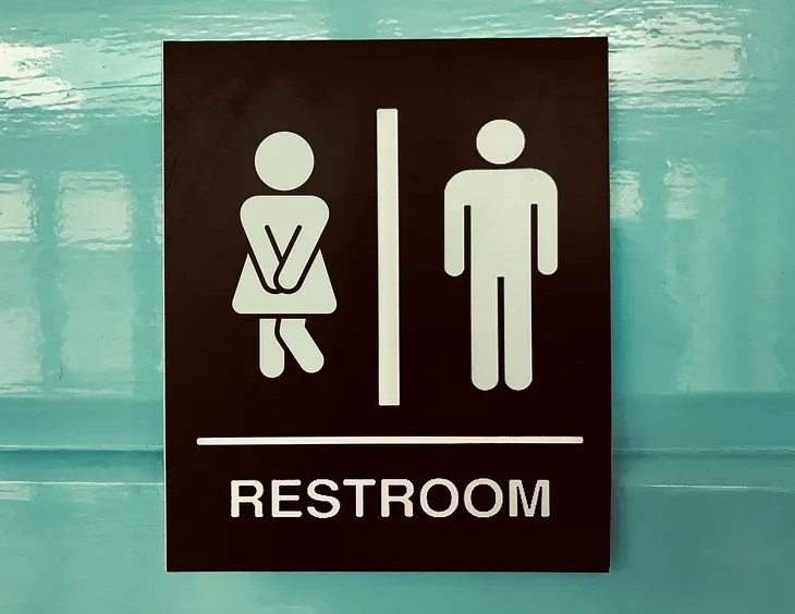 A restroom sign with a woman and man figure; woman is crossing her legs