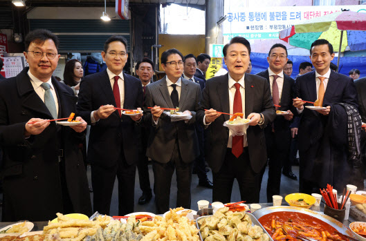 지난해 12월 6일 윤석열 대통령이 부산 중구 깡통시장에서 재계 총수들과 함께 떡볶이, 튀김, 빈대떡을 맛보고 있다. 연합뉴스