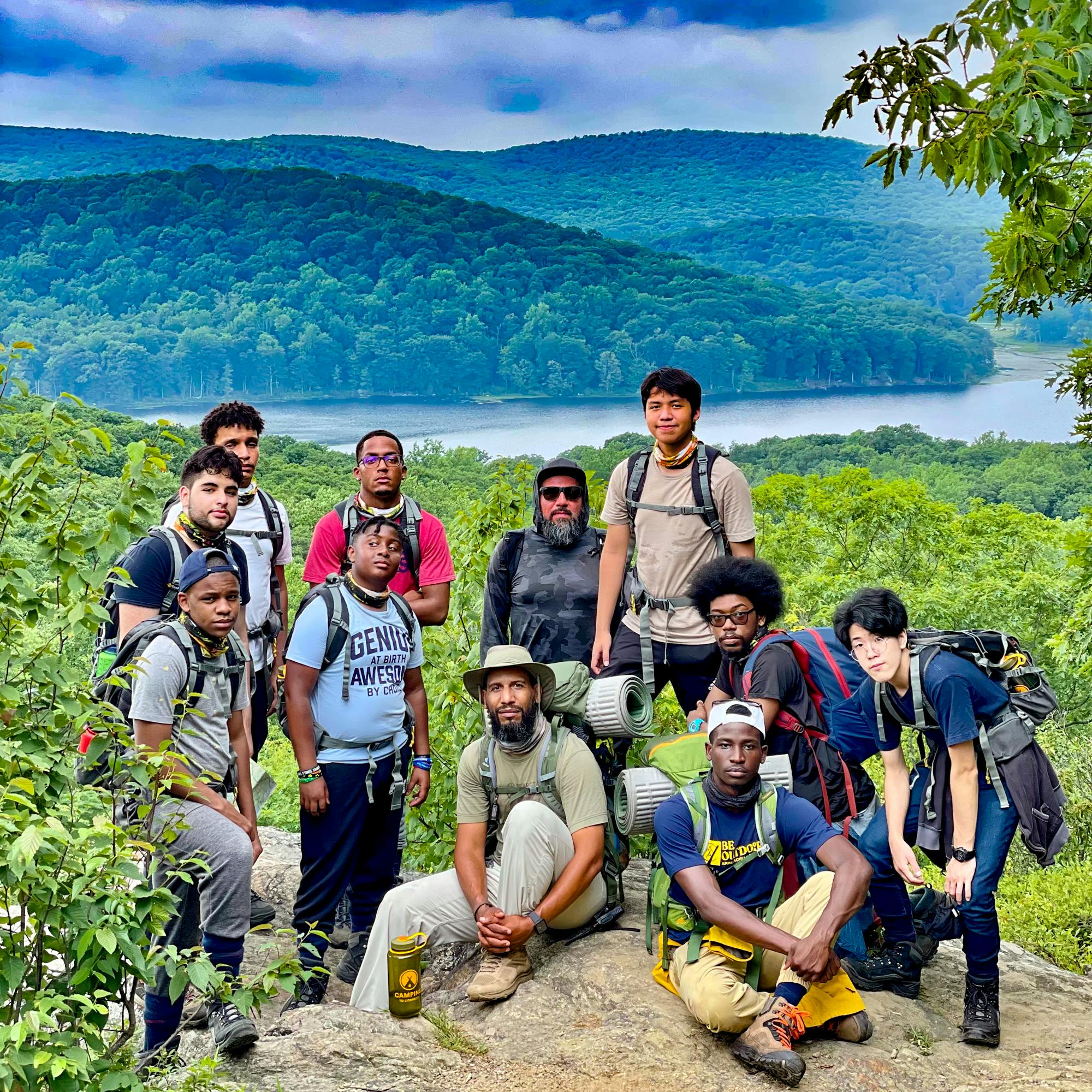 A group of men pose for a photograph with a grassy mountain range in the background