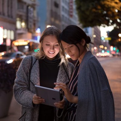 Two women use Surface Go on a dark street