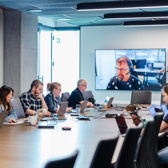 Employees working on their computers around a boardroom table.