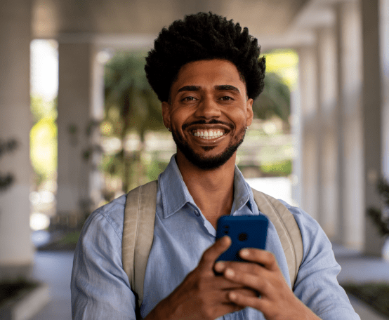 Homem com mochila nas costas mexendo no celular e sorrindo