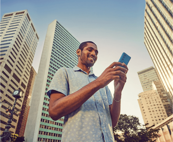 Homem ao ar livre mexendo em celular e sorrindo