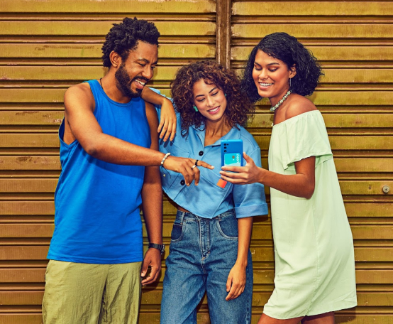 Um homem e duas mulheres olhando para celular, todos em frente a fundo amarelo