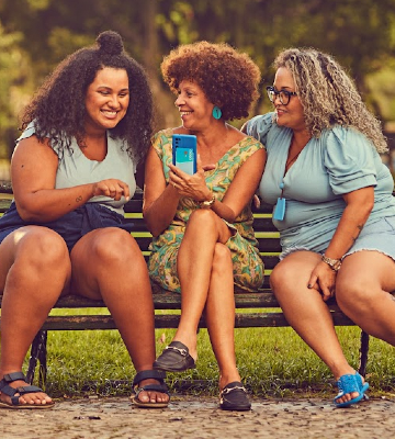 Mulher sorrindo segurando celular na mão em frente a fundo azul escuro