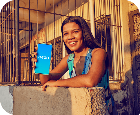 Mulher sorrindo em frente a a uma casa segurando celular em que se vê o logo Neon na tela