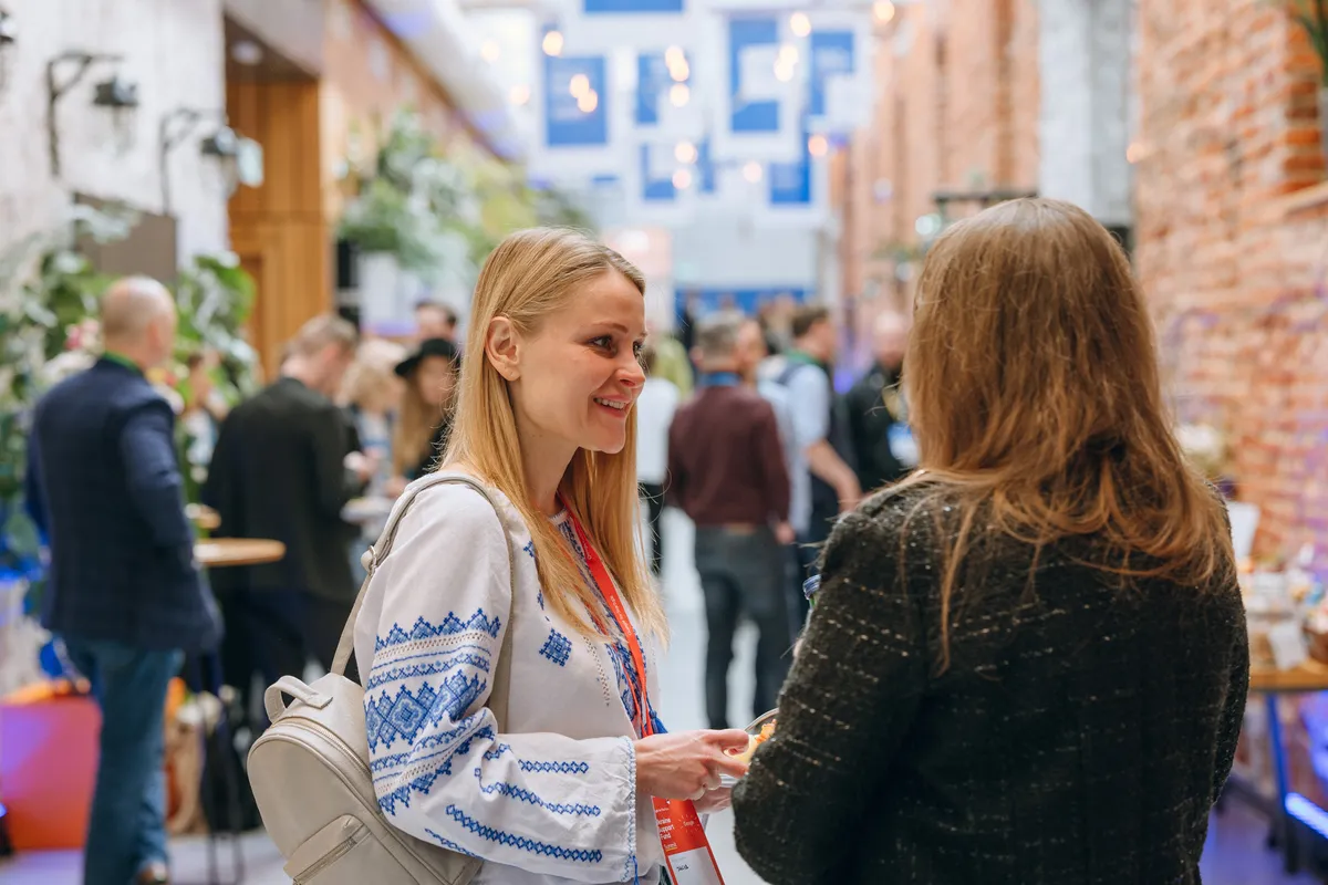 Two women stand in a open hallway; the woman on the left wears a traditional white and blue Ukrainian shirt.