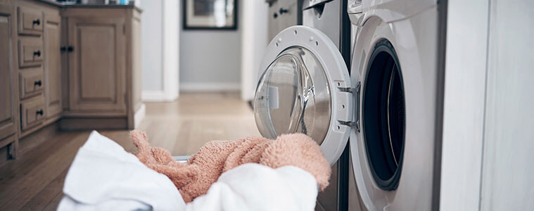 Laundry basket filled with freshly dried clothes on the floor in front of a dryer with the door open