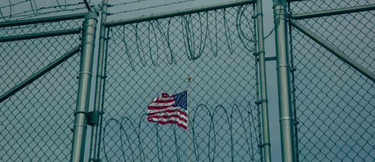 GUANTANAMO BAY, CUBA - JUNE 27: (EDITORS NOTE: Image has been reviewed by the U.S. Military prior to transmission.)  An American flag flies behind barbed wire fencing at the Office of Military Commissions building on June 27, 2023 at Guantanamo Bay, Cuba. At the prison within Naval Station Guantanamo Bay where media members are no longer allowed, 30 men still remain imprisoned while five separate war crime prosecutions involving some of the detainees proceed within Guantanamo's war court  none have yet reached a trial date. (Photo by Elise Swain/Getty Images)