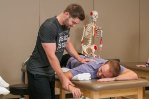 Student applying shoulder technique to another student on a treatment table