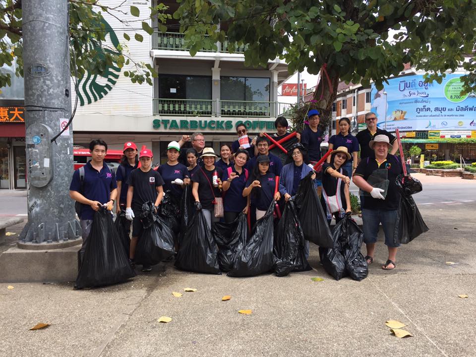 A group of people stand together holding full trash bags.