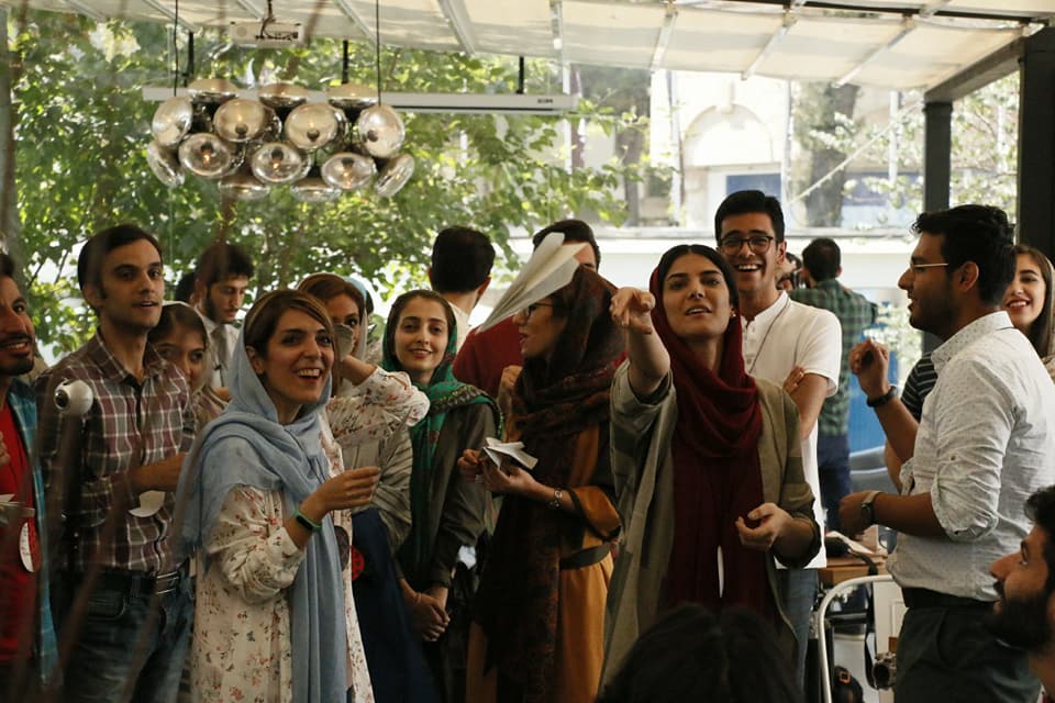 An energetic group of people. A woman in the middle throws a paper plane that is mid-flight.