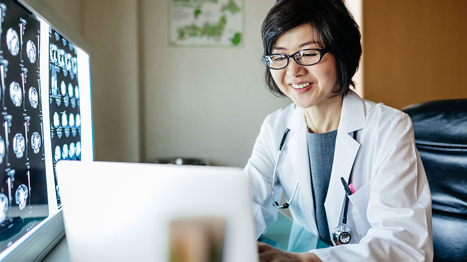 Doctor wearing glasses working on a laptop.