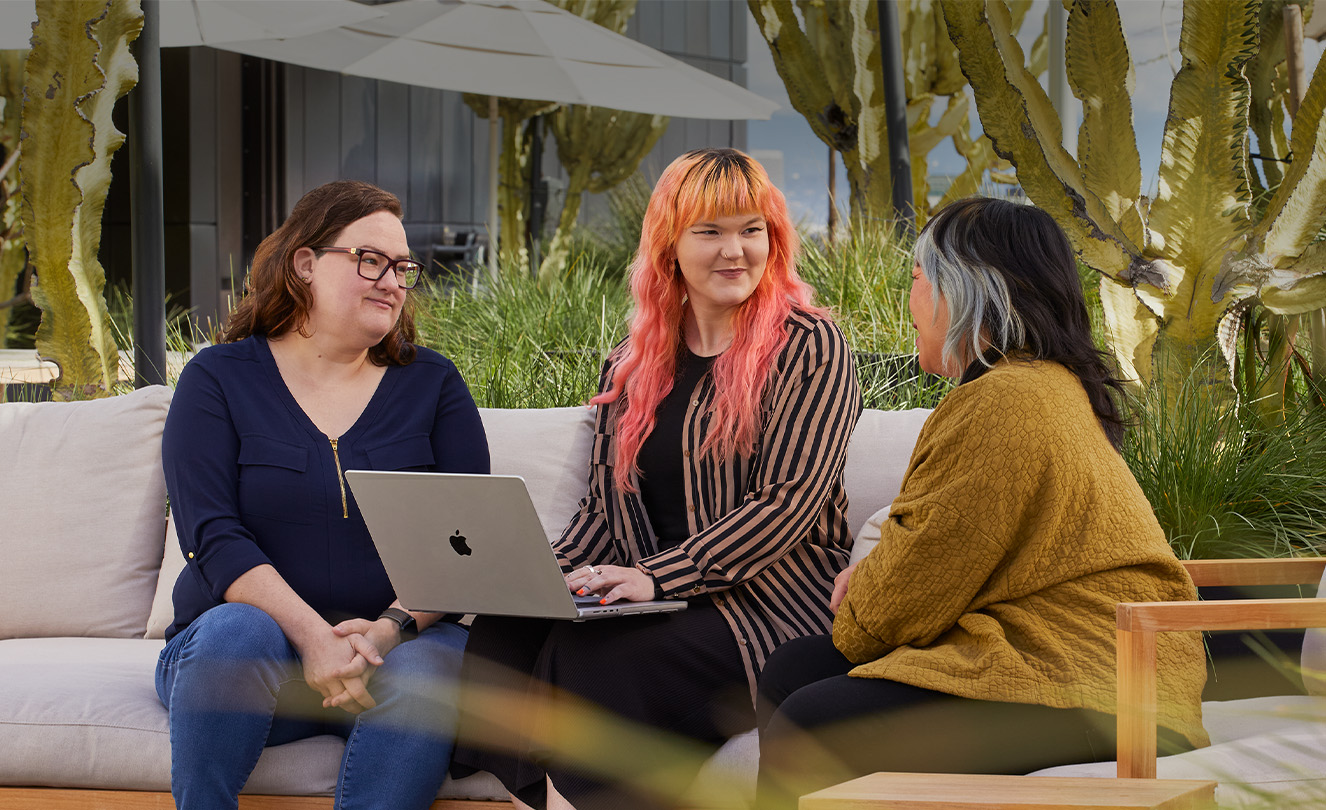 Drei Apple Teammitglieder sitzen zusammen auf einer Terrasse, eines mit einem MacBook.