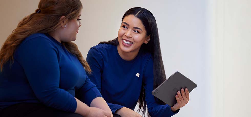 Carissa sostiene un iPad y habla con otra empleada de Apple Retail.