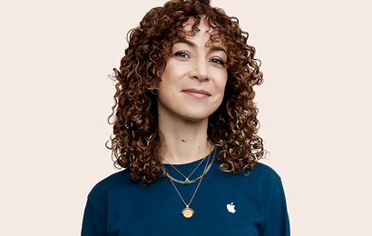 Empleada de Apple Retail con cabello rizado ve a la cámara.