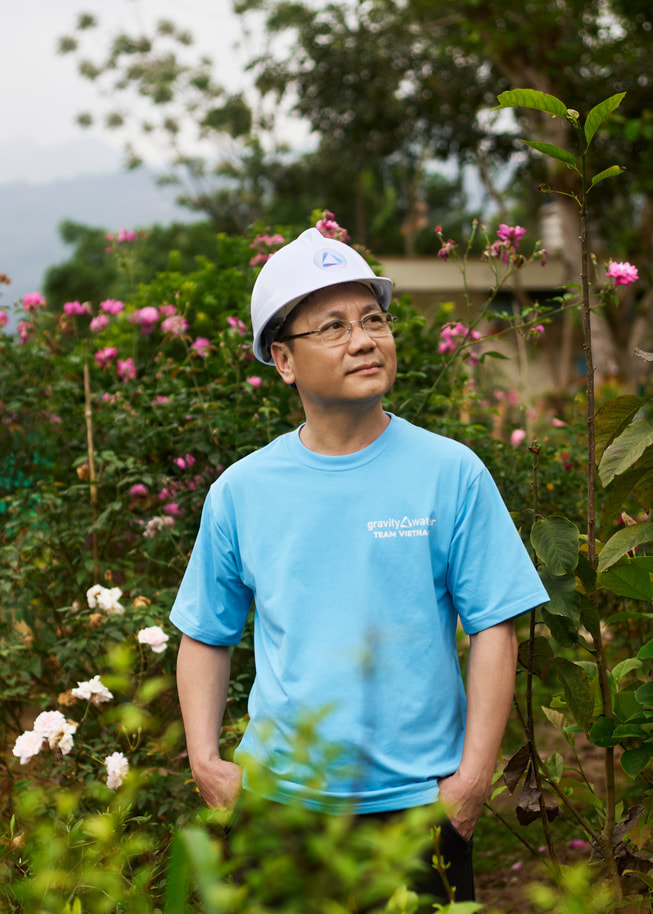 Ett porträtt av Phan Viet Dung som står utomhus med blommor bakom sig och med en skyddshjälm på huvudet.