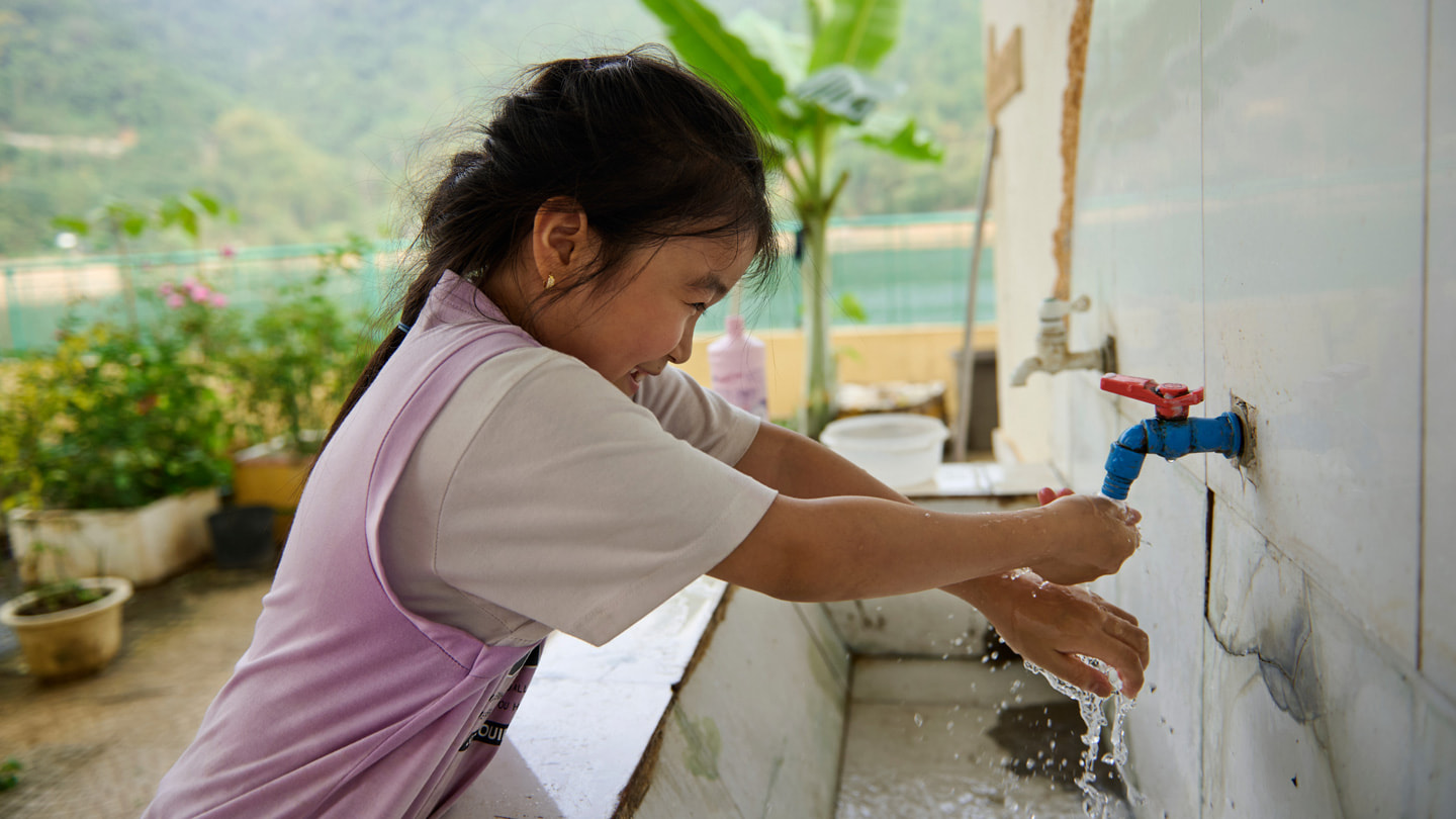 Un élève se lave les mains en extérieur dans une grande bassine munie d’un robinet à l’École primaire et secondaire Hiền Lương.