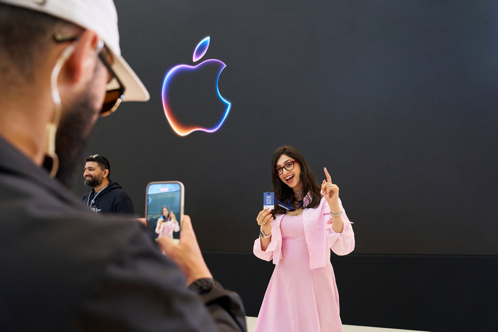 An Apple team member takes a photo of an attendee who poses with their badge for WWDC24. 