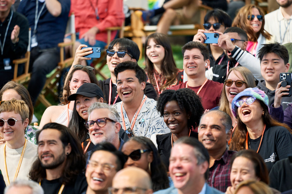 A close-up shows developers clapping, smiling, and holding up their iPhone devices while watching the keynote. 