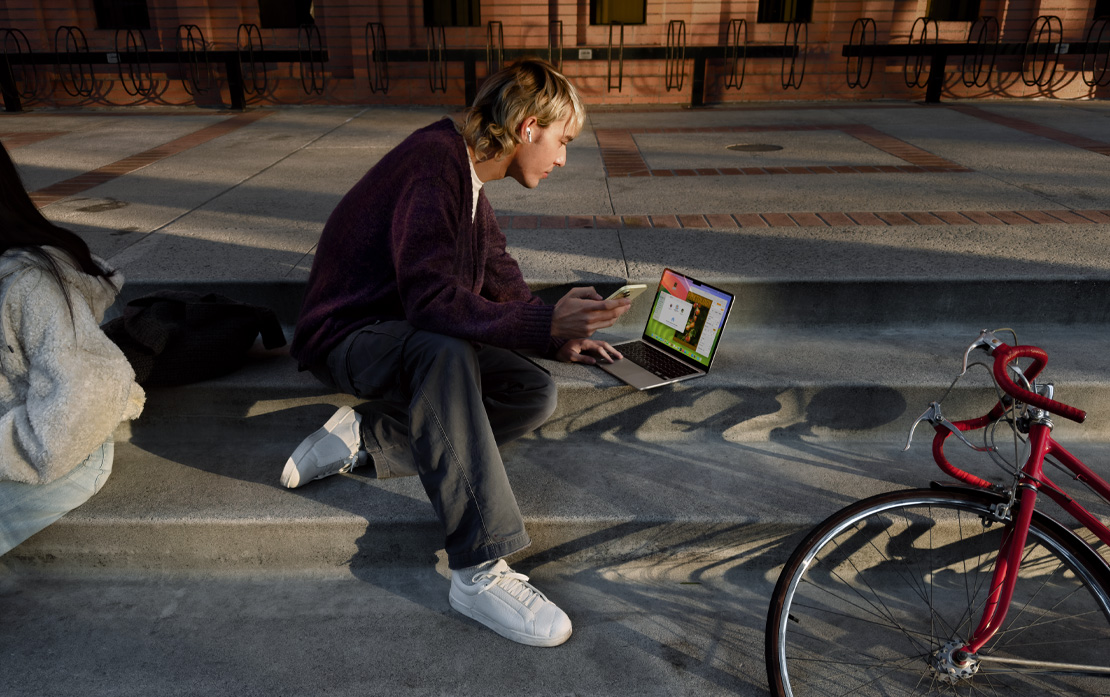 Studiująca osoba, która siedzi na schodach z rowerem i używa iPhone’a oraz MacBooka