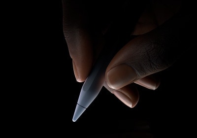 Seorang pengguna memegang sepertiga bagian bawah Apple Pencil Pro di antara ibu jari dan telunjuk, bersiap menulis.