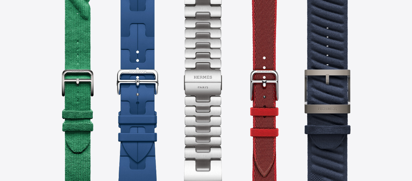 Vue montrant la face externe de cinq bracelets Hermès dont le Torsade rouge grenat, le Kilim vert moyen, le Grand H satiné (argent satiné), le Twill Jump Attelage simple tour rouge/vermillon (rouge avec bordure rouge) et le En mer bleu nuit.