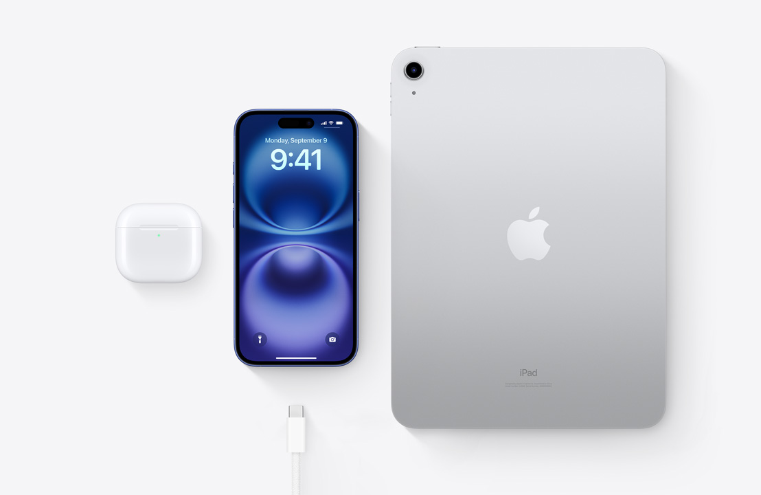 Lintuperspektiivistä kuvatut AirPods Pro -kuulokkeet, iPhone 15 ja iPad sekä USB-C-liitin. Niillä esitellään, miten kaikki kolme laitetta voidaan ladata samalla USB-C-johdolla.