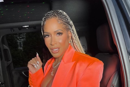 Sheree Whitfield in a bright orange blazer sitting in a car.