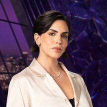 Katie Maloney wearing a white jacket with a black tank top in a purple room overlooking LA.