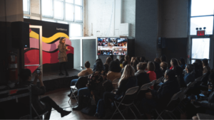 Event organizer speaks on stage while staff films on phone