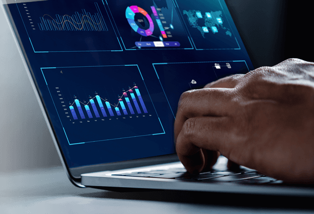 Stock photograph of a man's hands typing on a laptop, with the laptops screen showing general analytics and data visualization