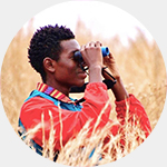 Isaiah Scott sitting in a grassy field looking through binoculars.