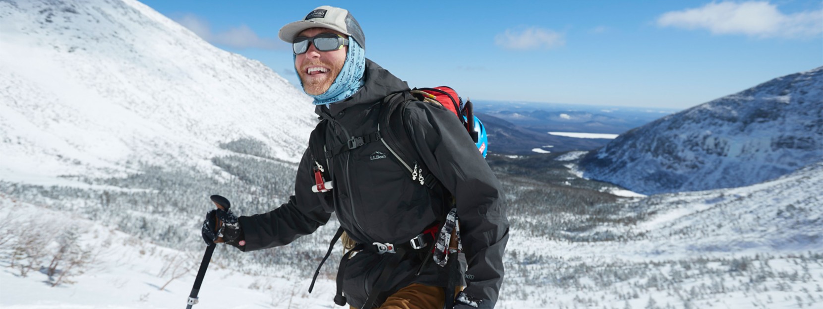 Man outside in the mountains in winter wearing a backpack and carrying a hiking pole.