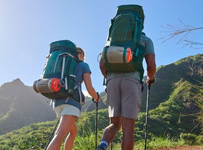 2 hikers wearing large packs and using hiking poles, shot from behind, beautiful mountain scene and blue sky.