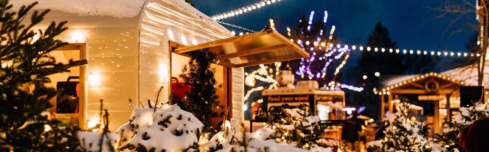 The snow-covered hot cocoa cabin at night surrounded by twinkling lights.