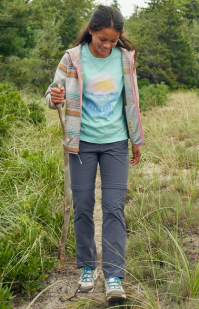 Young girl walking on a grassy trail holding a walking stick.