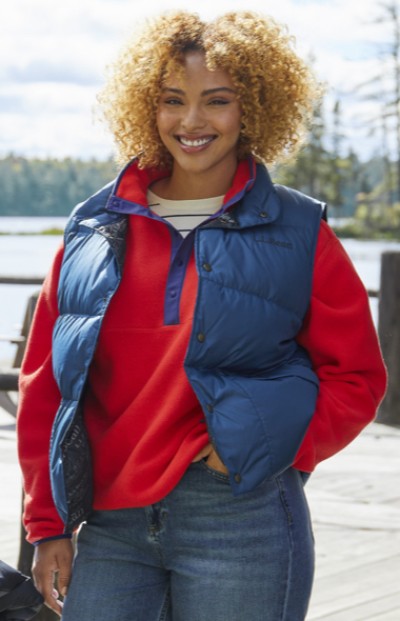 Woman wearing a vest with a lake in the background.