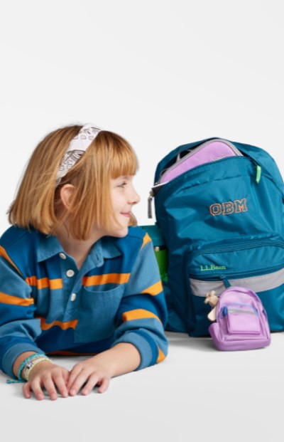 A young girl on the floor looking at her school backpack and accessories.