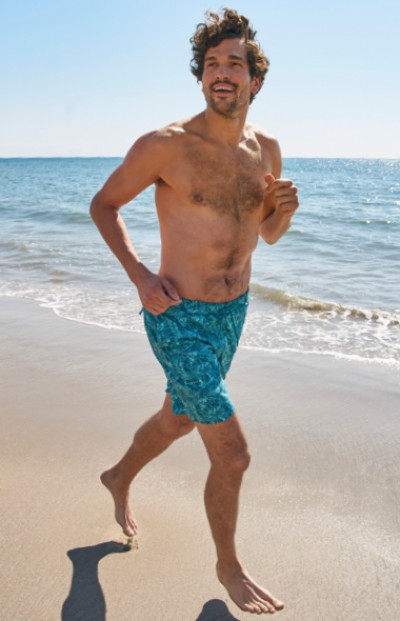 A man runs on a beach, with waves and a clear sky in the background.