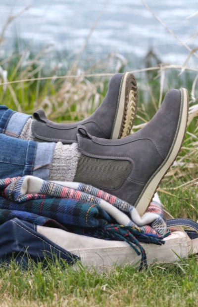 A person wearing boots rests on a plaid blanket on grass, suggesting a cozy outdoor setting. 