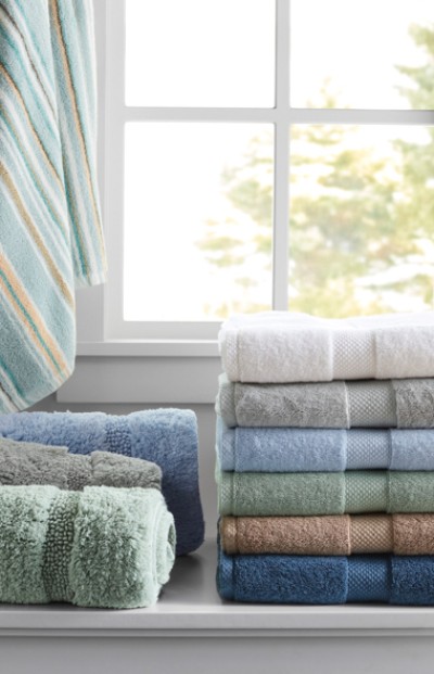 Stacked colorful L L Bean towels by a window with a view of trees, showcasing variety and home organization.