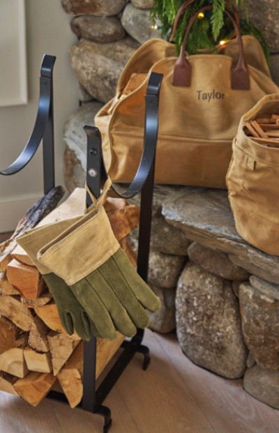 A fireplace set with gloves, wood, and a personalized bag rests by a stone hearth, creating a cozy and prepared atmosphere for a warm fire.