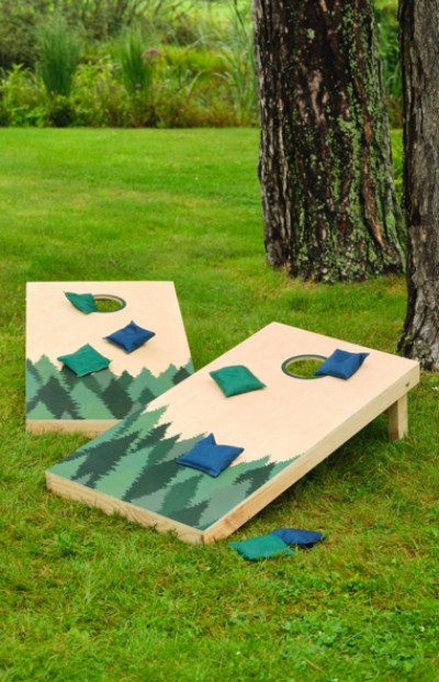 A L L Bean cornhole game set on grass, with one board leaning against a tree and bags scattered around it. 