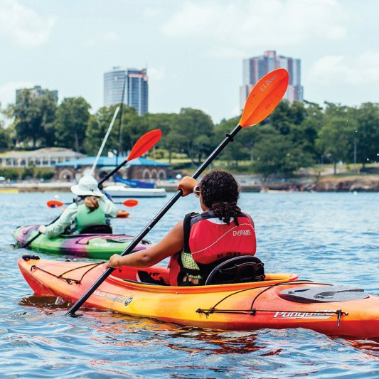 A group of kayakers paddling with a cityscape in the background.