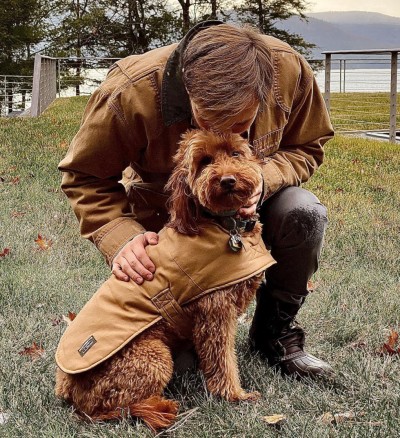 A man wearing a Field Coat bends to pat a dog wearing a dog field coat.