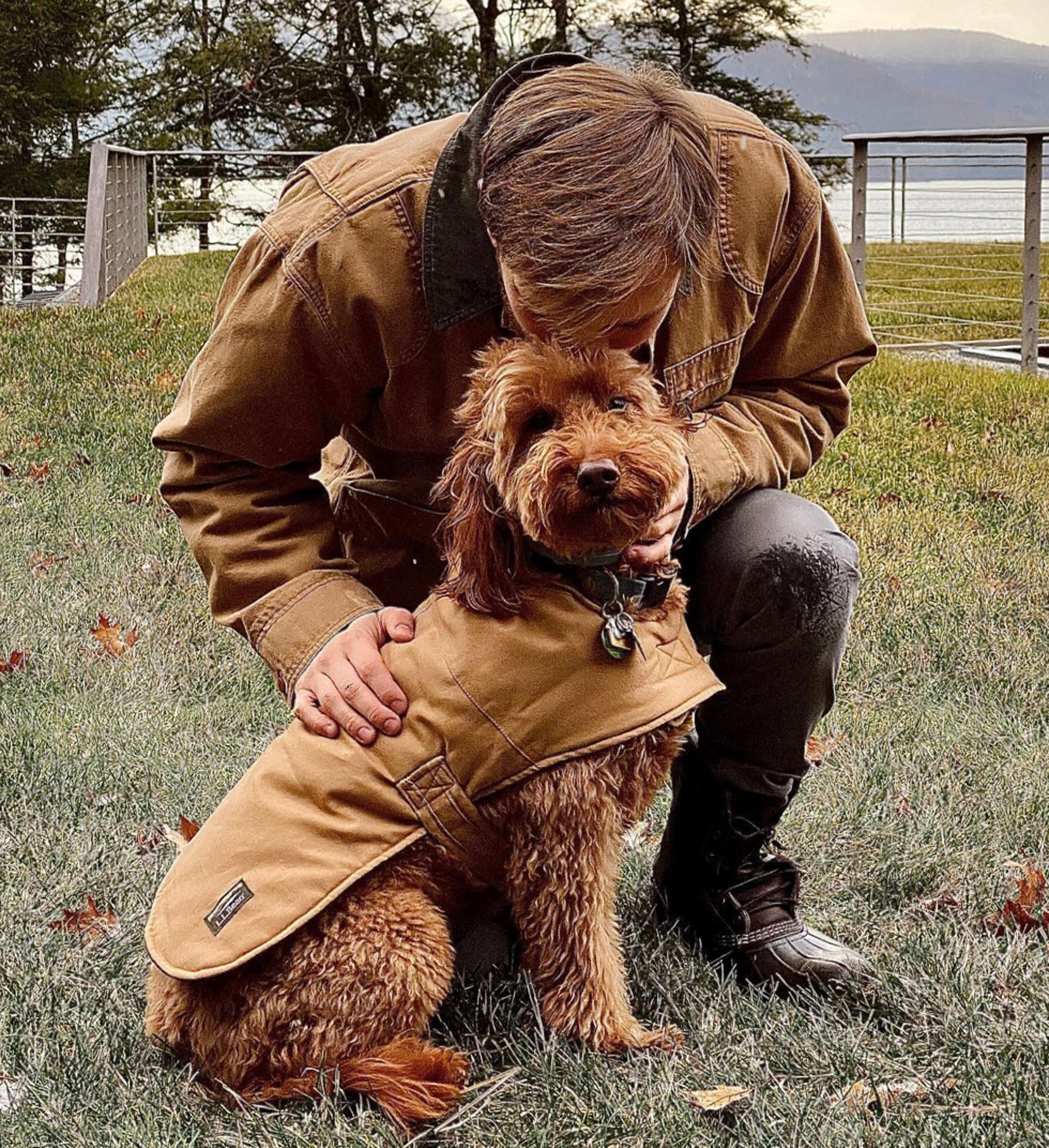 A man wearing a Field Coat bends to pat a dog wearing a dog field coat.