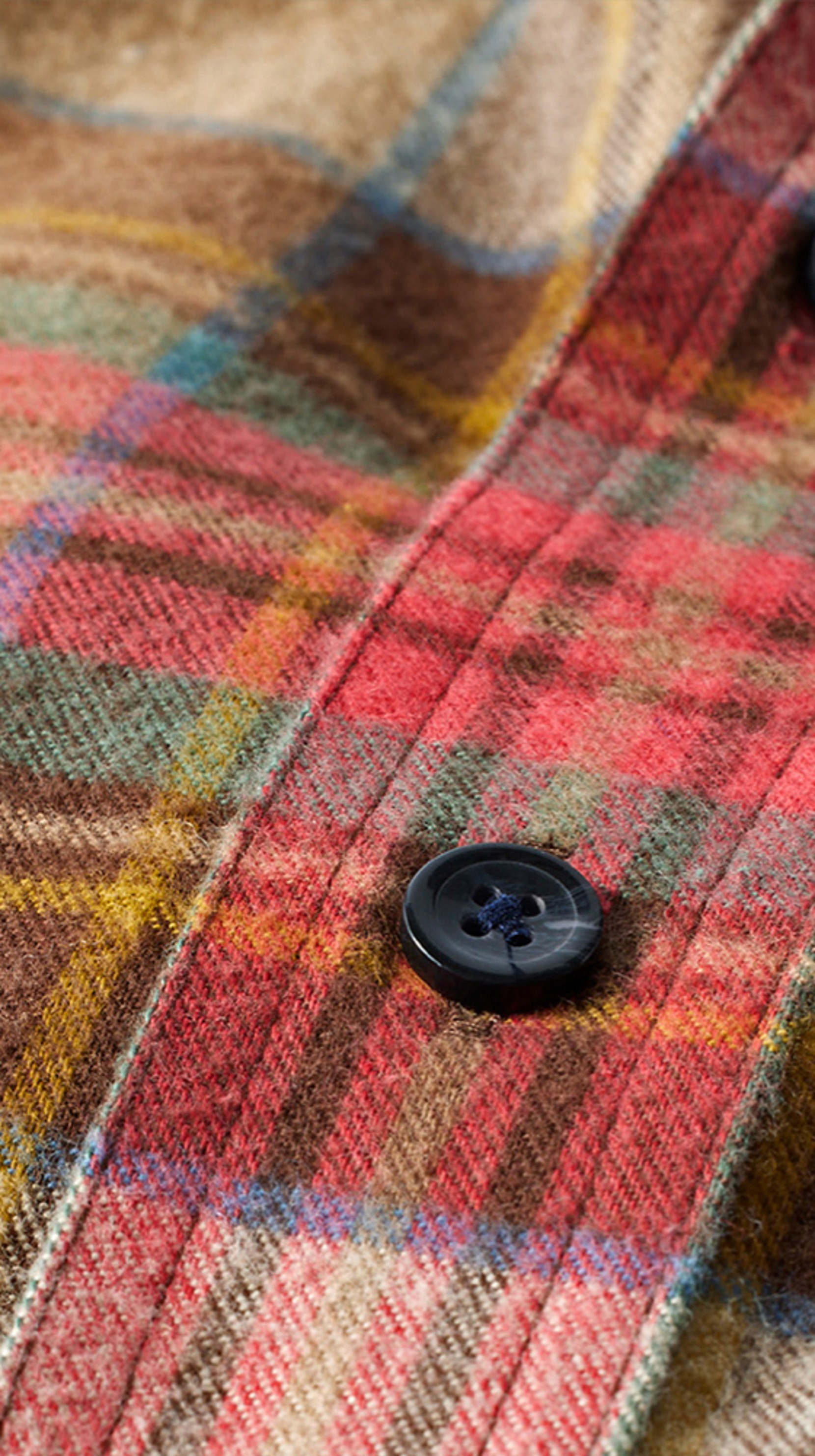 Close up detail shot of plaid flannel fabric with two black buttons, showcasing texture and pattern.